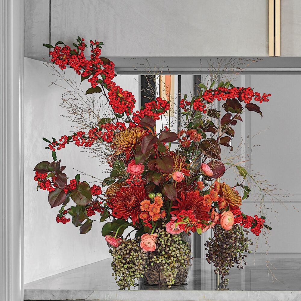 Arrangement of red pyracantha berriese, red and gold mums, green berries, grasses, and coral ranunculus.