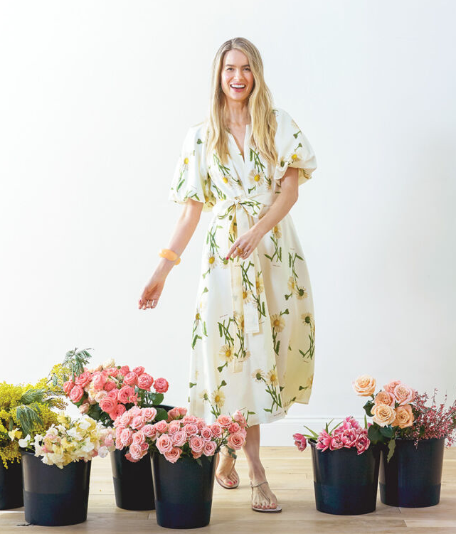 Alice Callahan Thompson wearing floral print silk dress, standing with buckets of flowers on floor.