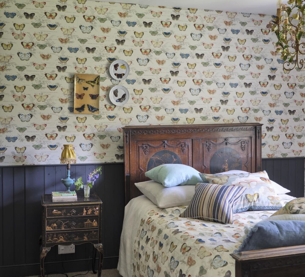 Bedroom with antique bed and dark wainscoting with John Derian for Designers Guild Butterfly Studies wallpaper on wall.