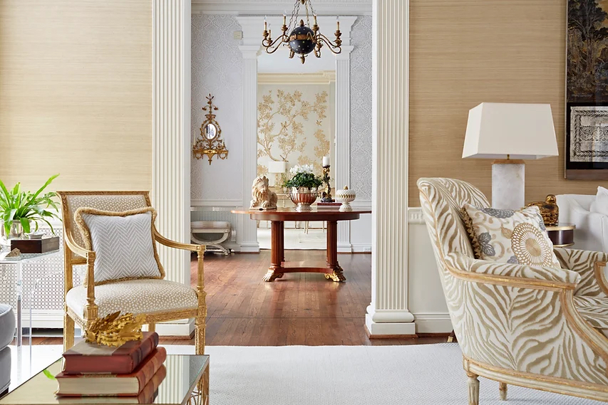 Living room with gold accents and grasscloth wallpaper, with doorway open into foyer and doorway to dining room beyond.