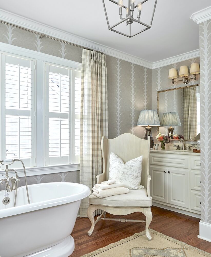 Bathroom with free-standing tub and queen Anne chair, vinyl grasscloth wallpaper on walls.