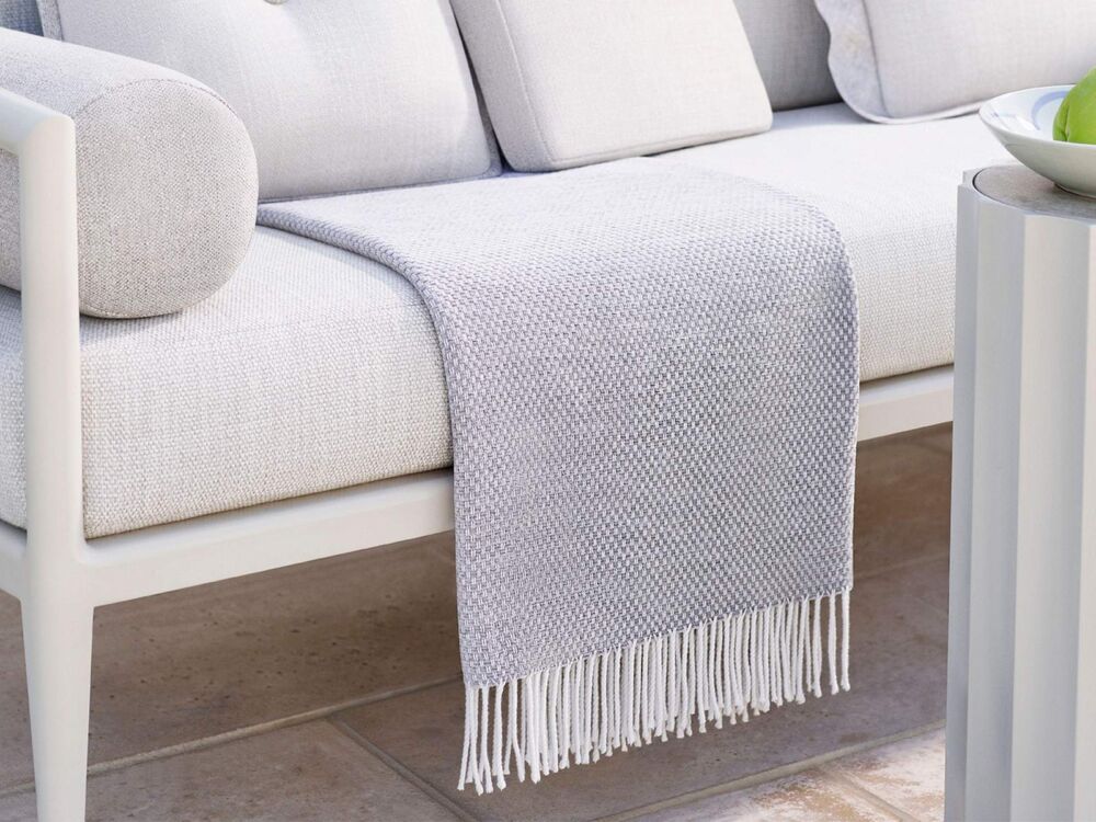 A grey blanket by McKinnon and Harris is folded on a white outdoor couch.