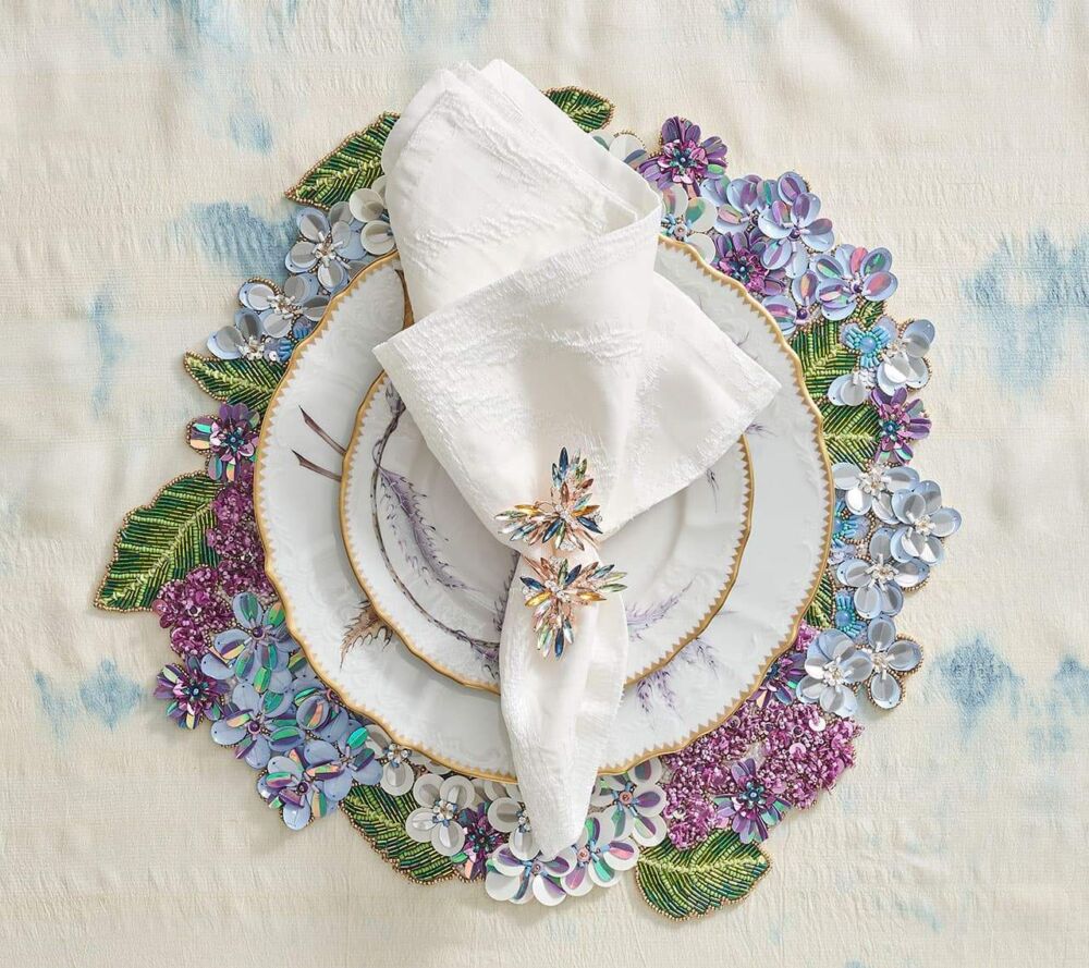 Bejeweled butterfly napkin ring holds together a white napkin on a gold rimmed plate.