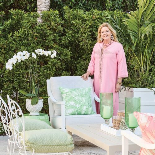 Meg Braff standing on patio with white orchids and outdoor furniture in green and white.