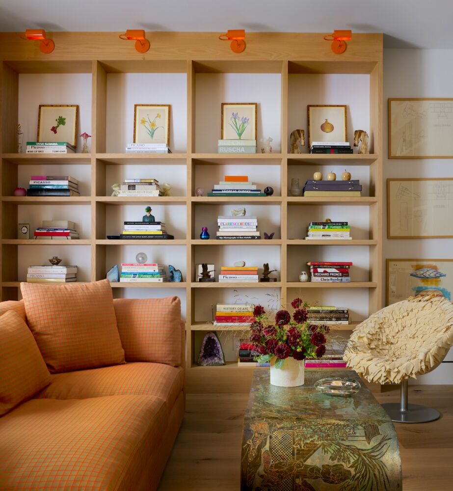 Bookshelves topped with orange sconces in room with orange sofa.