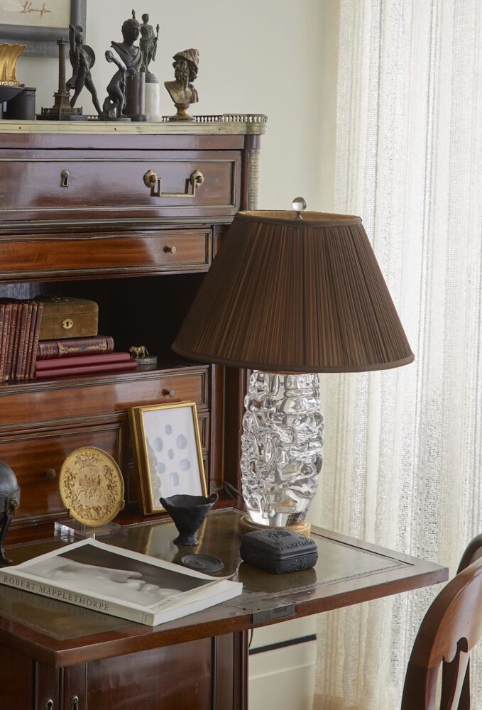 Wooden, folding front desk with book and crystal lamp topped by brown silk lamp shade.