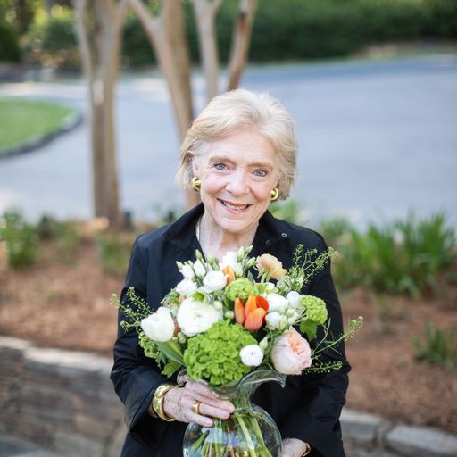 Susan Gravely holds a bouquet of greenery and peach and white roses in a glass Vietri vase.
