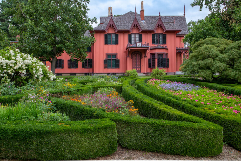 A bright red Victorian house sits behind a winding garden of green hedges at historic Roseland Cottage from Connecticut Gardens
