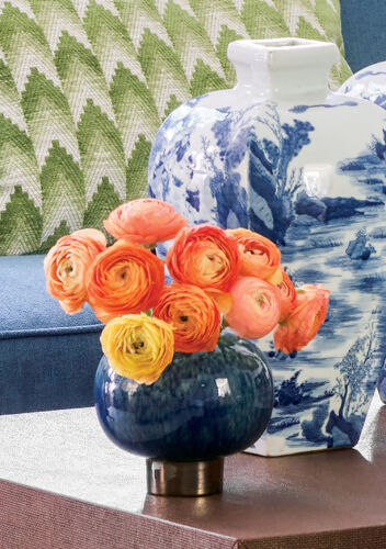 Bright orange ranunculus sit next to blue and white vases on a coffee table.