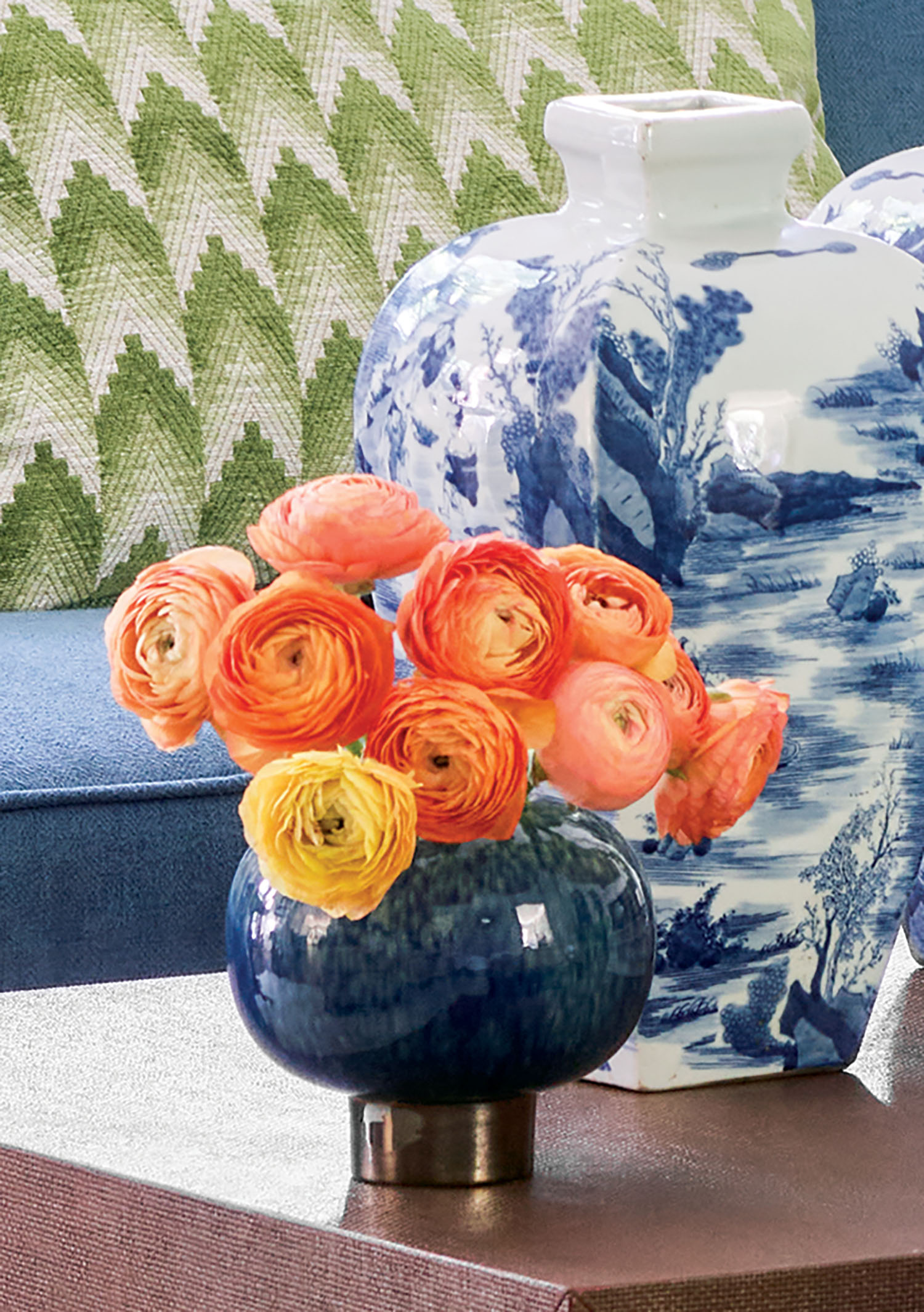 Bright orange ranunculus sit next to blue and white vases on a coffee table.