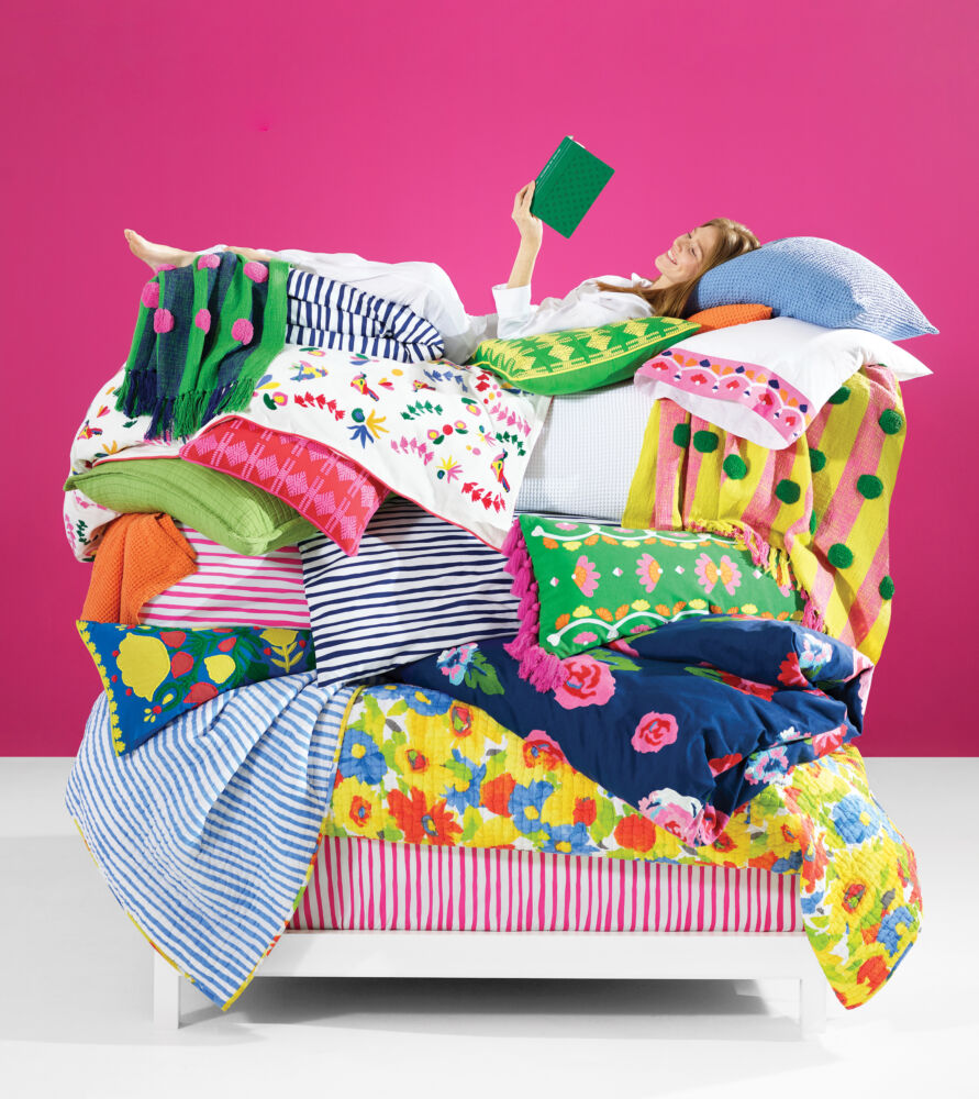 Like the princess and a pea, a girl lays on top of a mountain of bright floral pillows and blankets while reading.