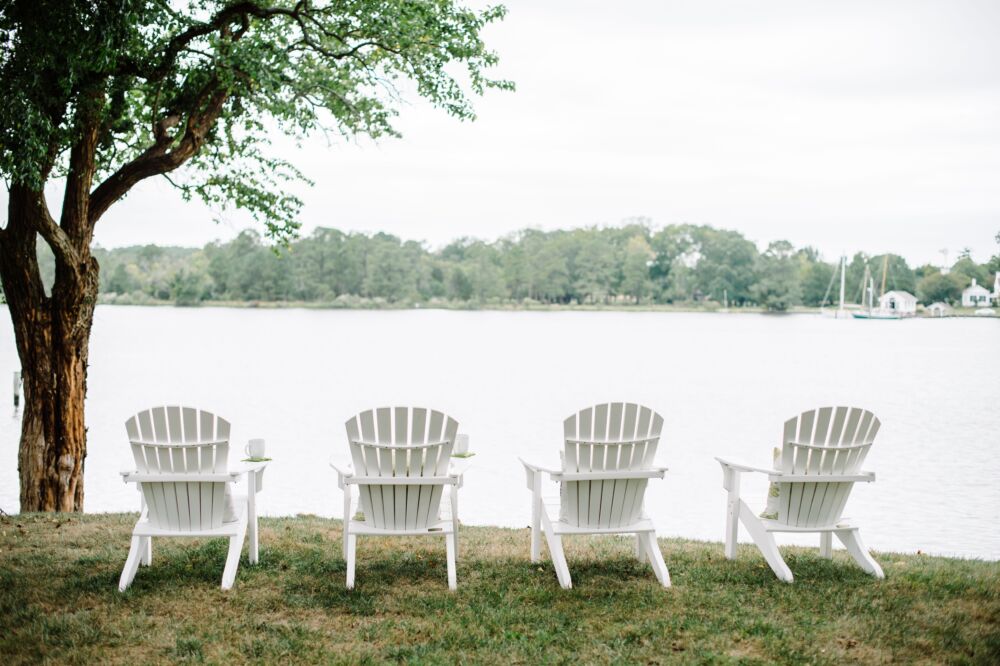 Four white Adirondack chairs sit overlooking a grey lake.