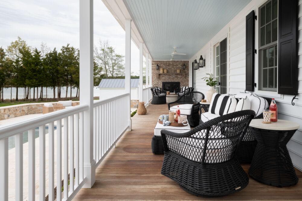 Black and white outdoor seating look out onto a lake and pool on a wooden wrap around porch.