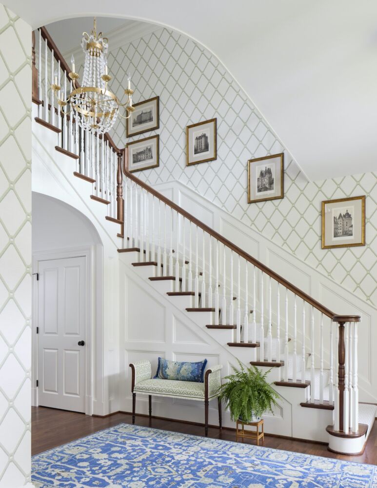 Stairway in a foyer with an elegant chandelier and a trellis-patterned Thibaut wallpaper in the Kelley Proxmire designed space.
