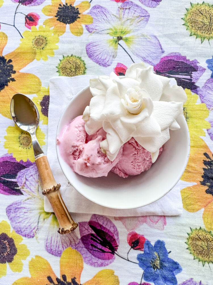 Pink strawberry ice cream sits in a bowl with a white gardenia.