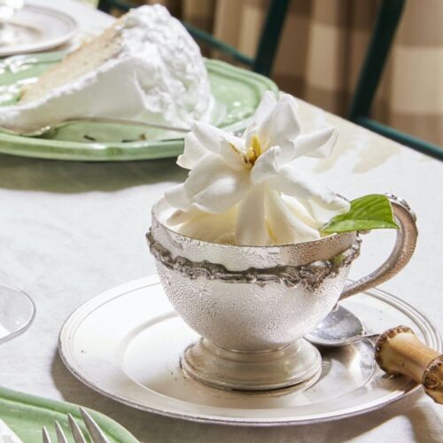 A large fluffy gardenia sits atop a dollop of vanilla ice cream in a silver tea cup.
