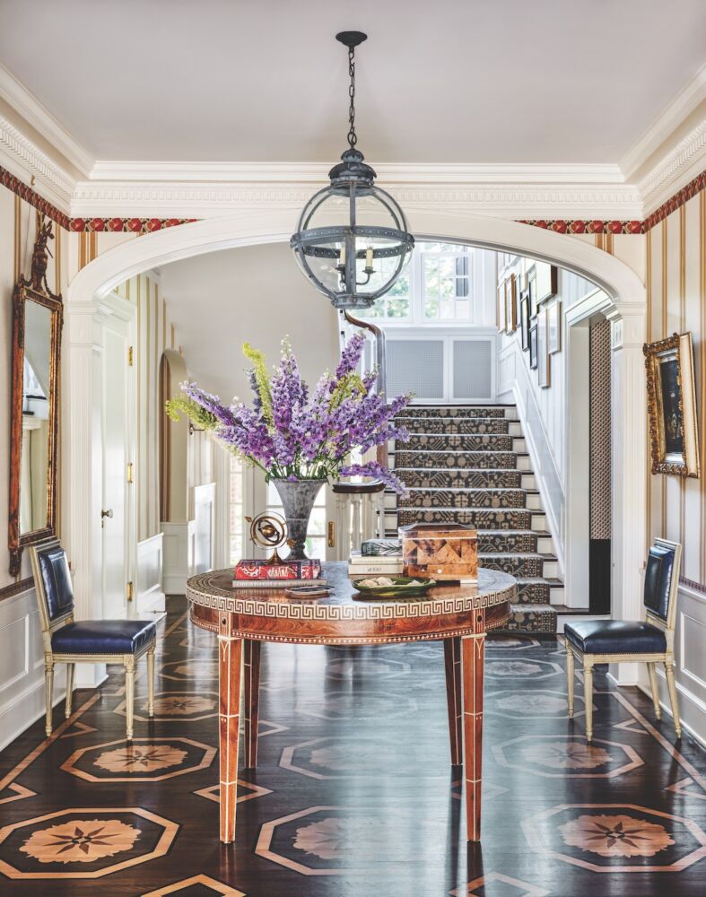 Foyer with wood floors painted to mimic marquetry. Round hall table topped with vase of delphiniums and eremurus.