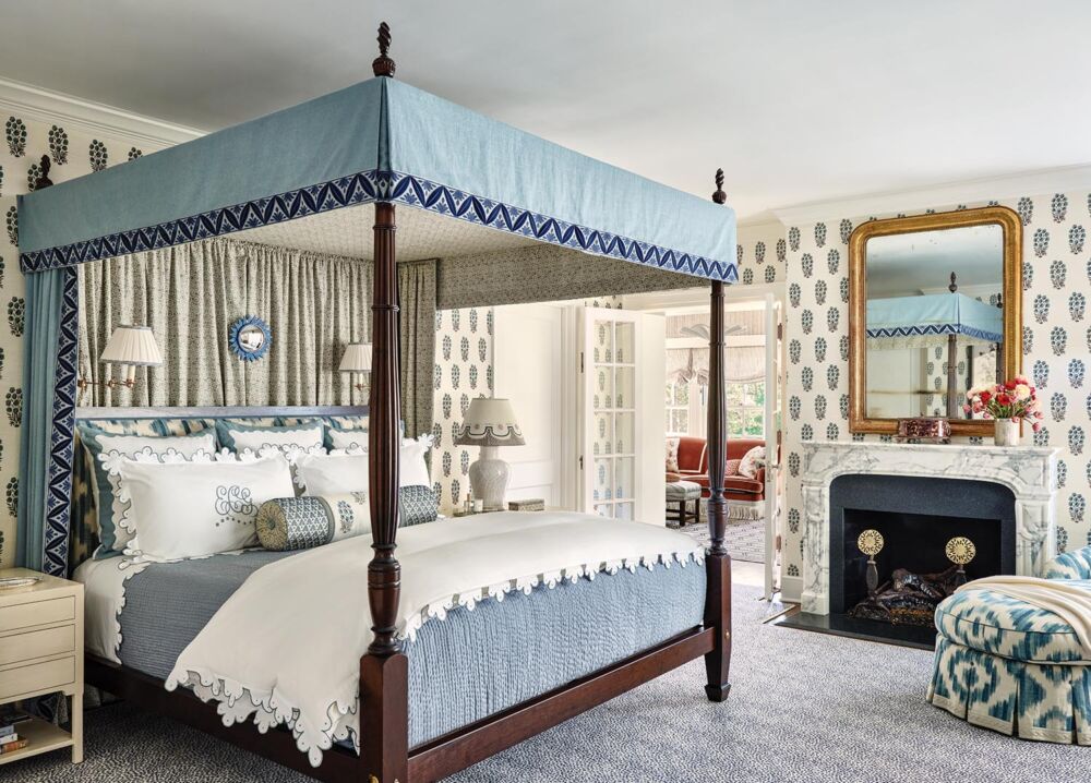 Primary bedroom with fresh floral prints in crisp whites and shades of navy, cobalt, and cornflower on a canopy bed. Louis Phillippe-style mirror, and marble mantel.
