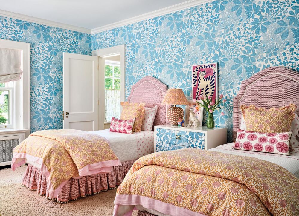 Bedroom with Marthe Armitage floral in blue and white covering the walls. A pair of beds with pink headboards flank a chest.