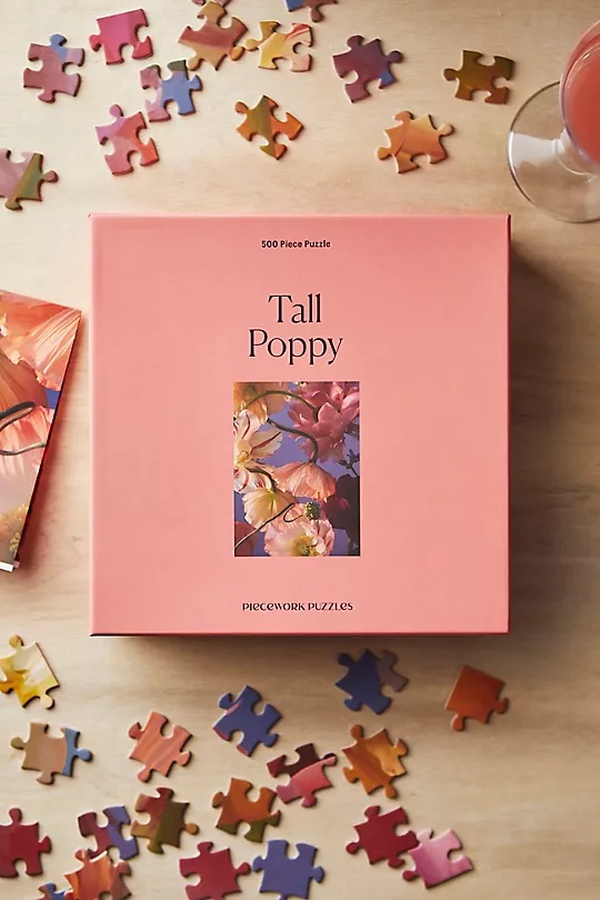 Piecework Tall Poppy puzzle box on tabletop with puzzle pieces