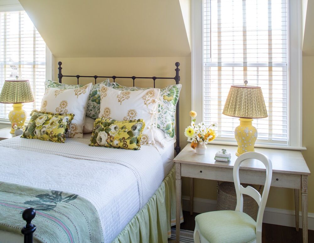 Yellow bedroom with bed between dormers and flanked by tables with yellow lamps. Walls painted Farrow and Pale Hound