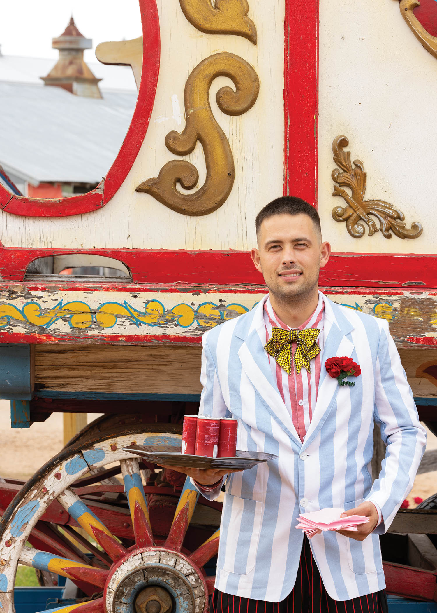 Man stands in front of a colorful carriage in a pale blue striped blazer.