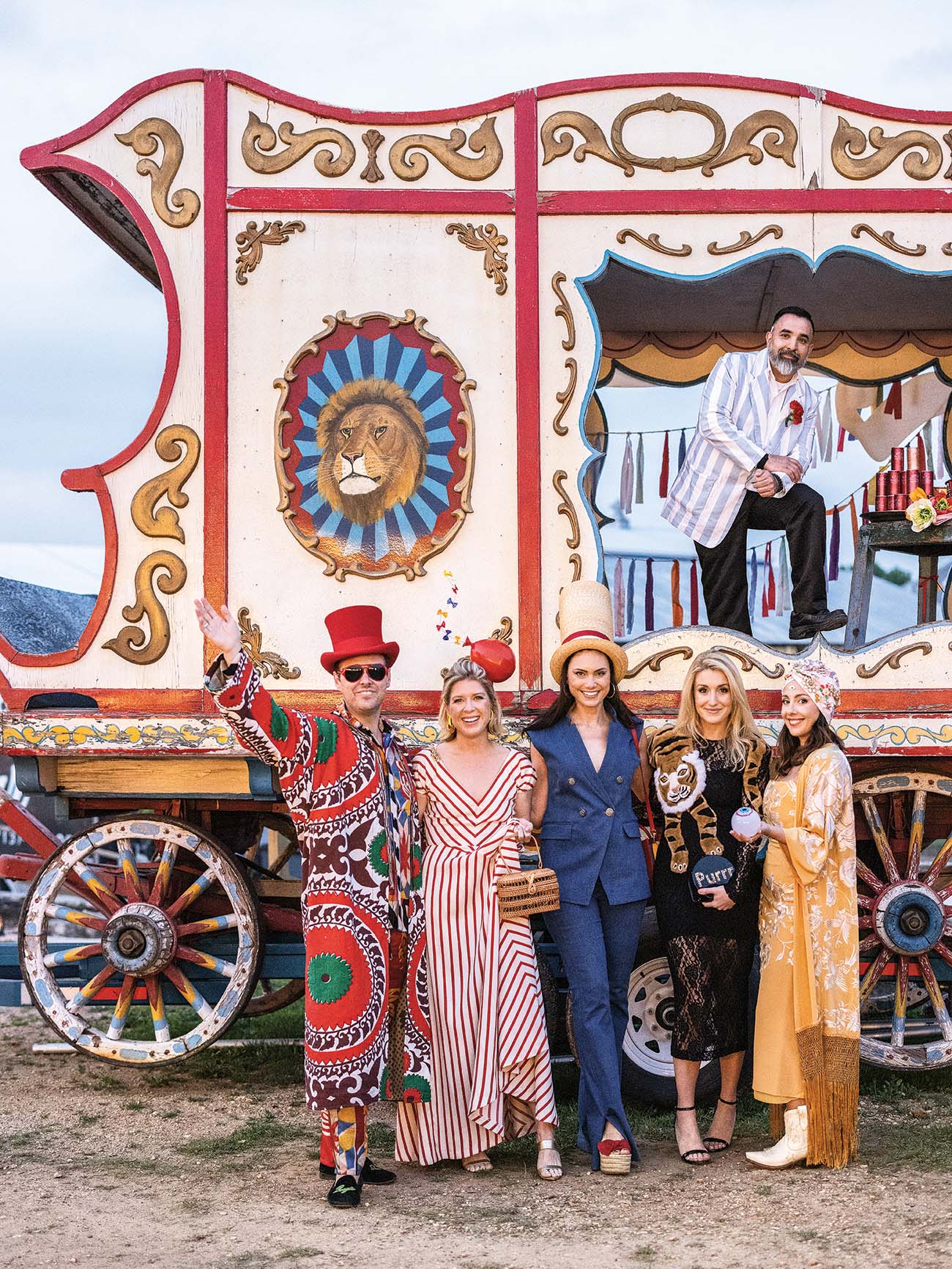 Gypsy dressed partygoers stand in front of a colorful caravan.