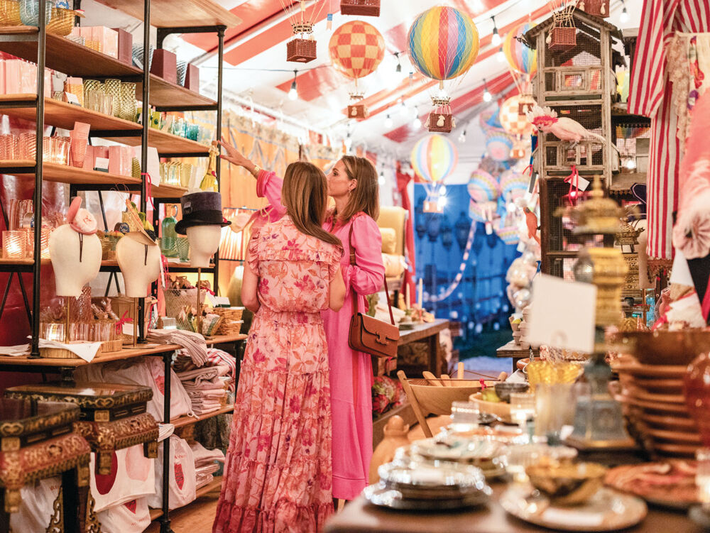 Two women in pink dresses browse antique home goods.