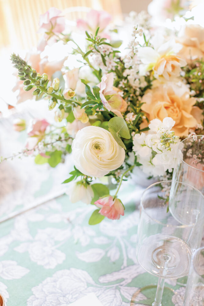 White ranunculus, foxgloves, hellebores, heather, and assorted white flowers pop against the green-and-white botanical tablecloth.