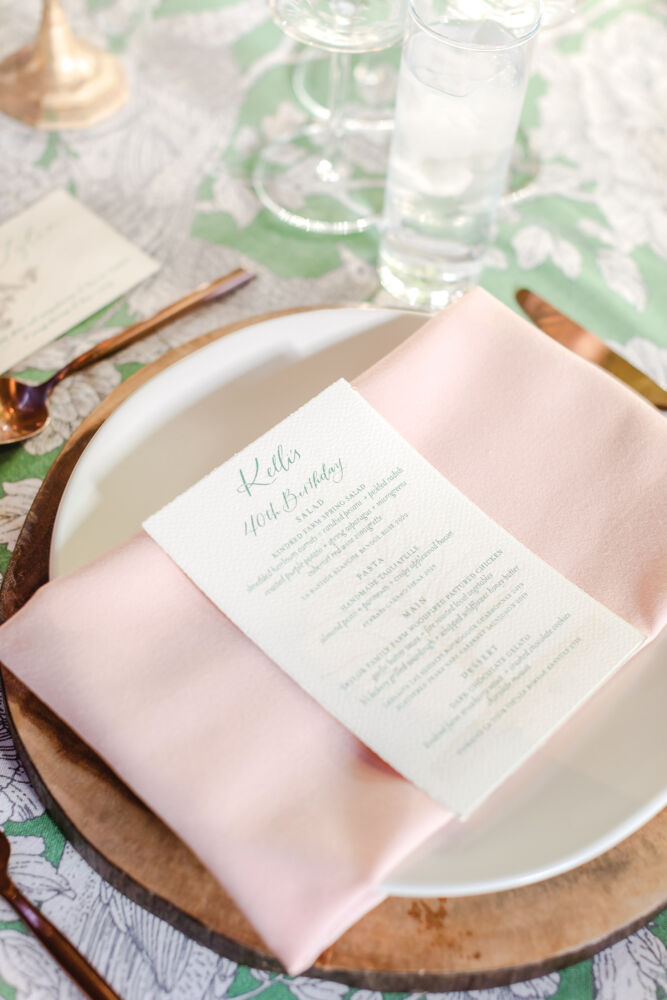 A menu with green ink sits on top of a princess pink napkin.