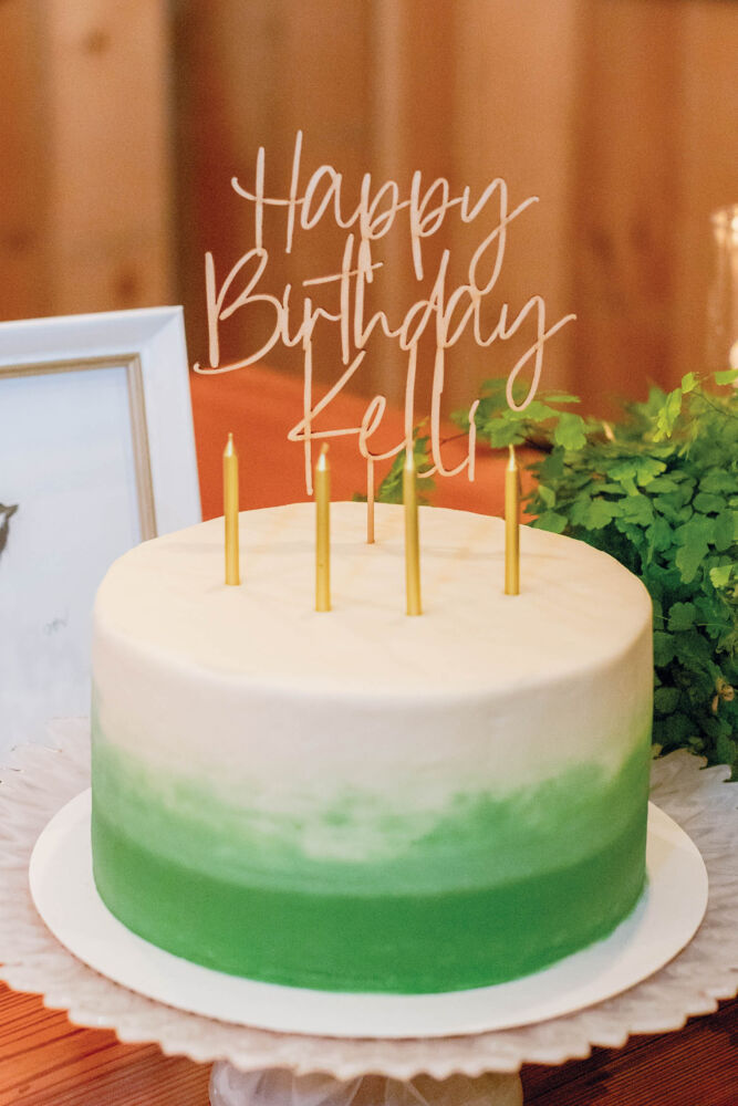 A green and white striped cake has candles and a Happy Birthday Kelli sign on it.