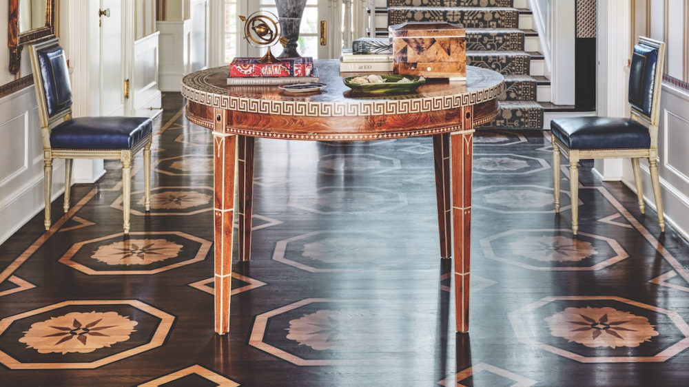 Painted floor in foyer with round table flanked by two chairs upholstered in blue leather.