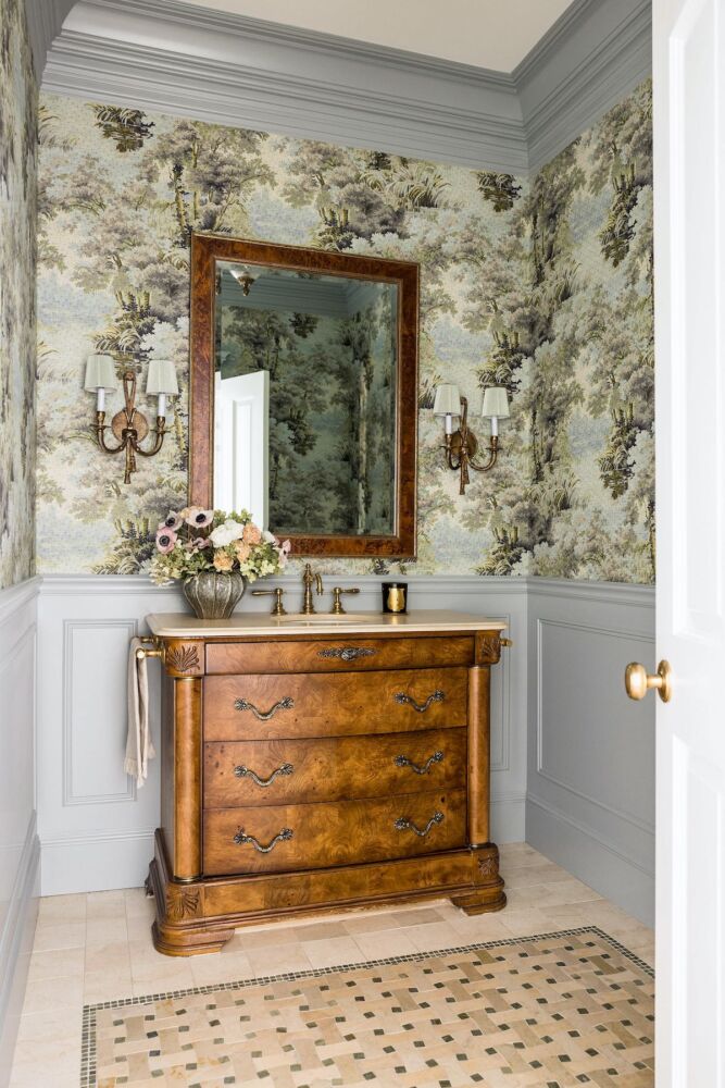 Powder room with green, large-scale Gucci botanical wallpaper above wainscoting. Antique chest adapted for sink holds a vase of anemones, hydrangea flowers and ranunculus.