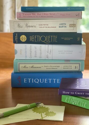 Stack of etiquette books on desk with notecard and pen. 