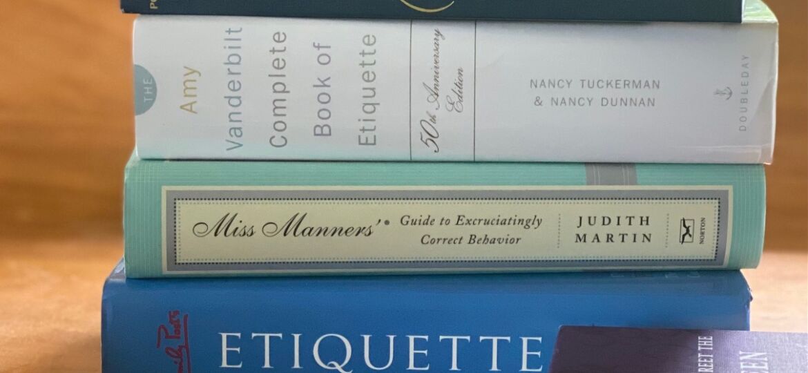 Stack of etiquette books on desk with notecard and pen.