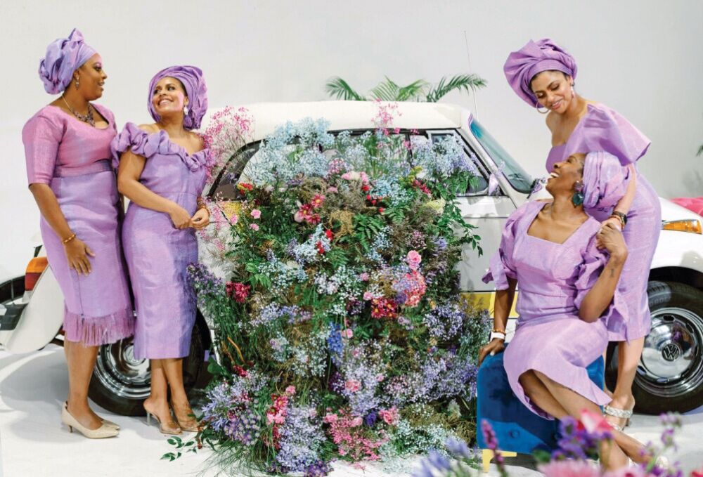 Four family members dressed in purple laugh together in front of a flowered car.