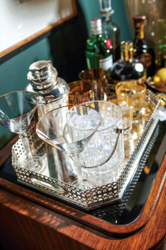 Cocktail glasses and liquors sit next to one another on a silver drink tray.