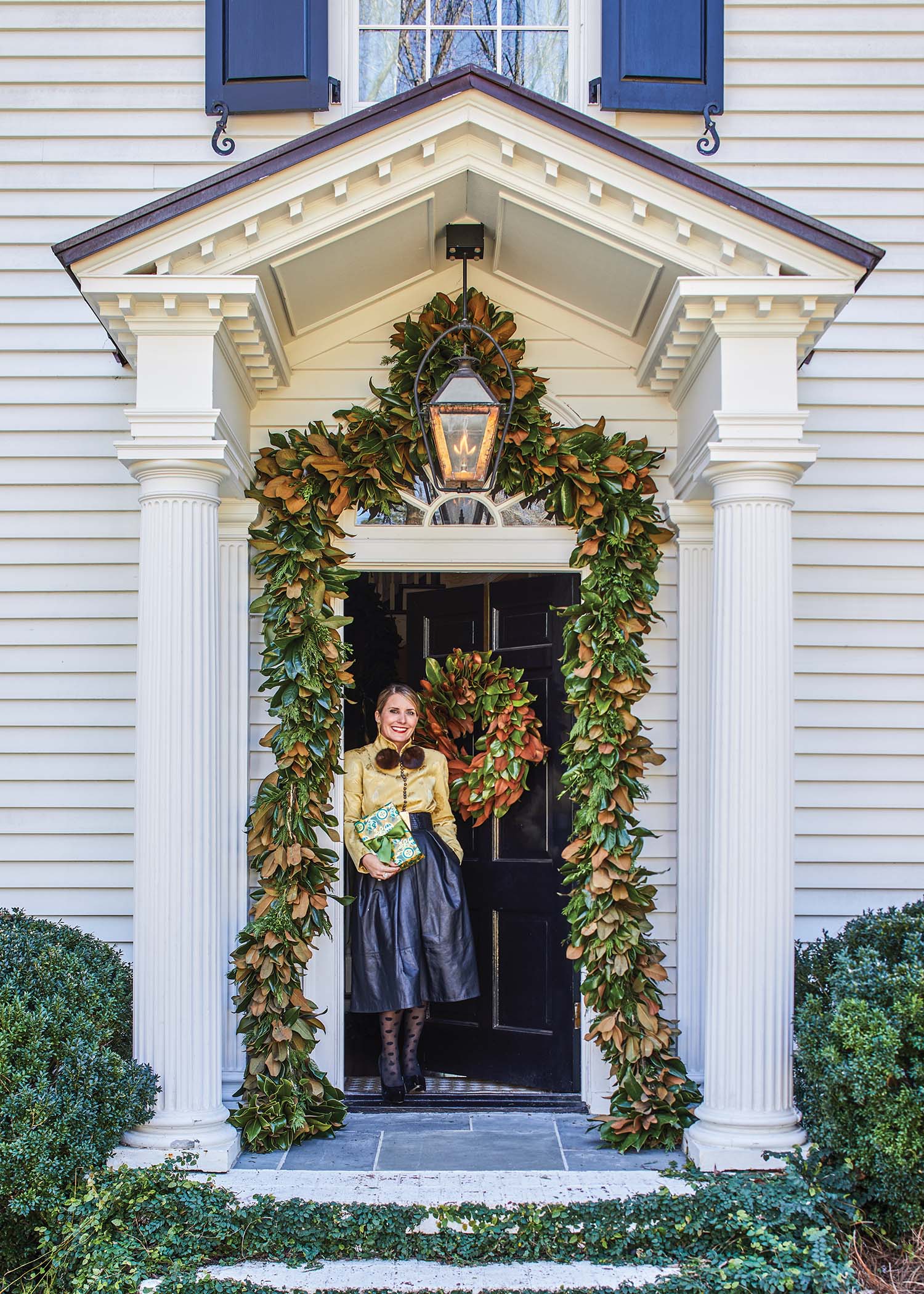 Danielle Balanis stands in her front door that's decorated with a wreath and a magnolia leaf garland.