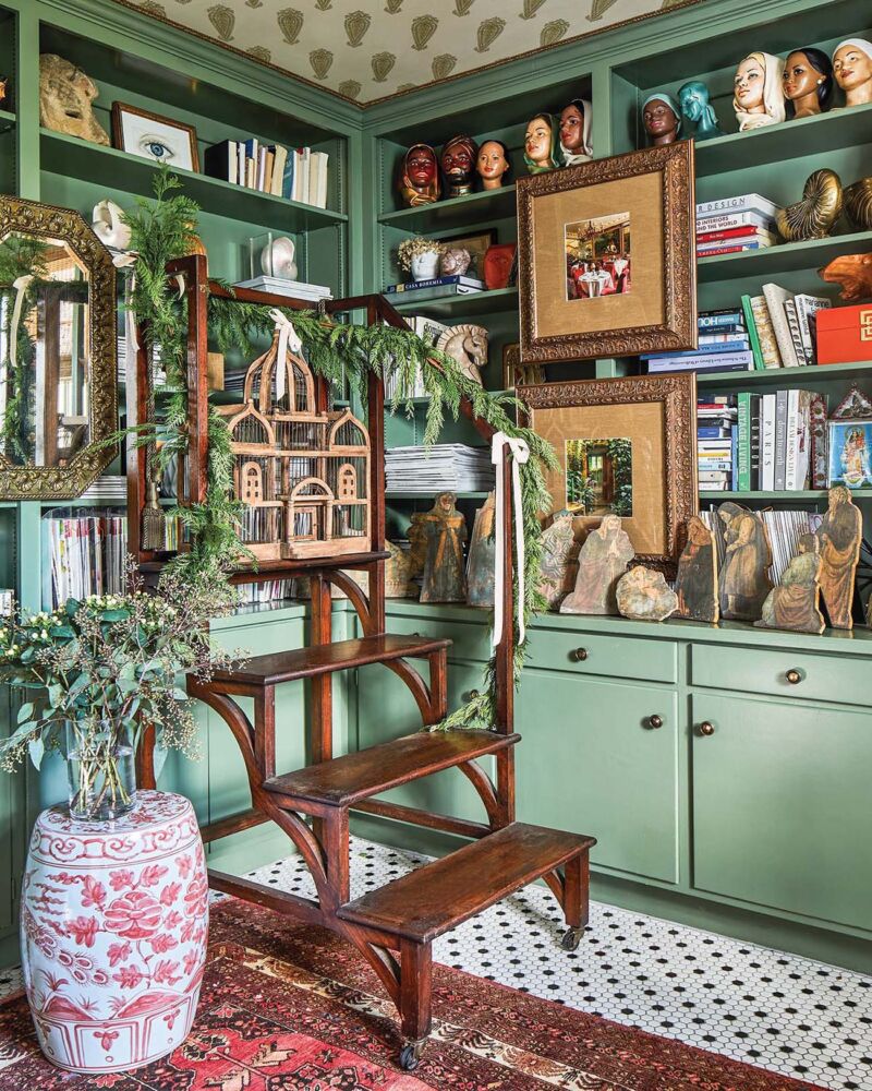 Green bookshelves are filled books and antiques.