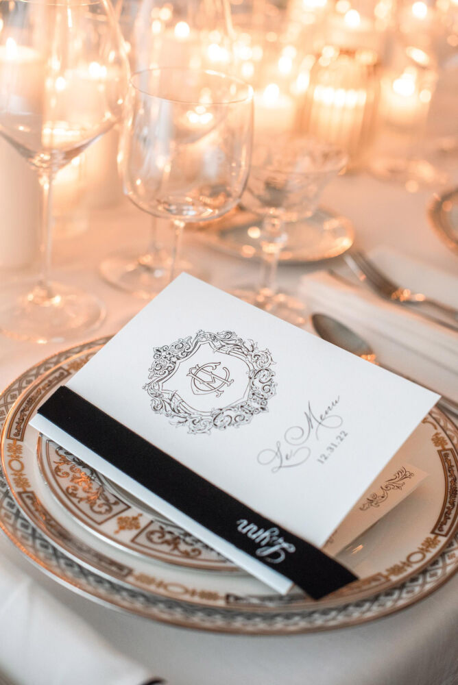 A menu with a black ribbon sits on gold rimmed china.