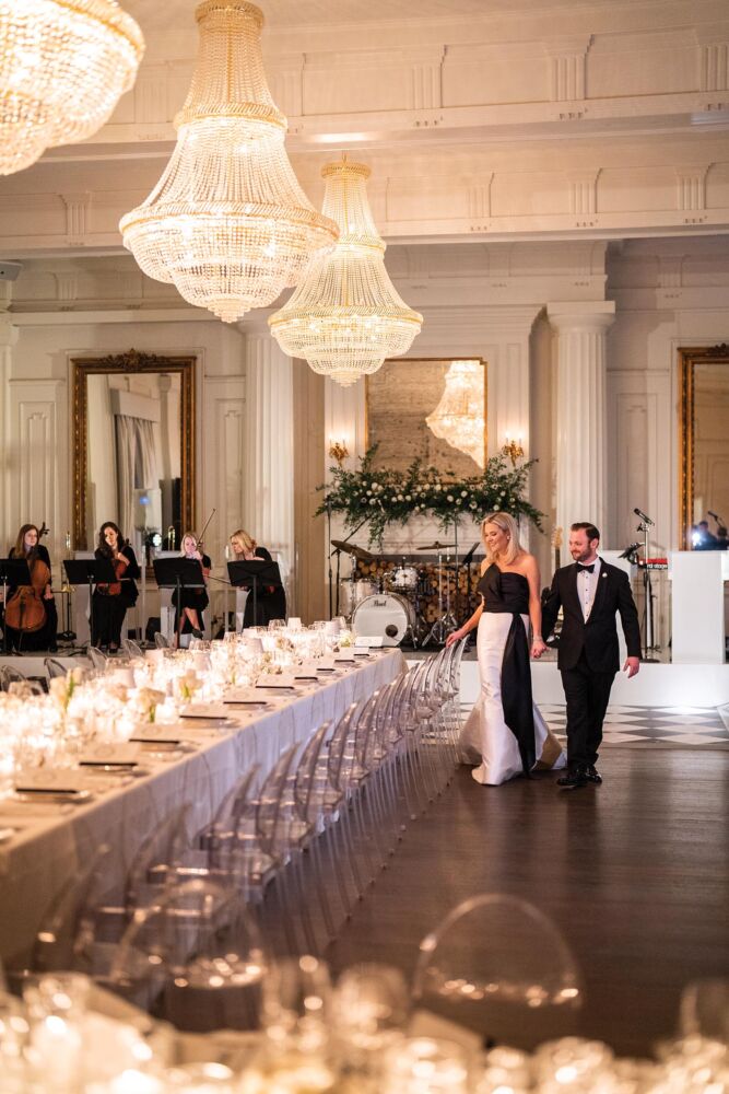 Bride and groom hold hands as they walk into the candlelit dining room.