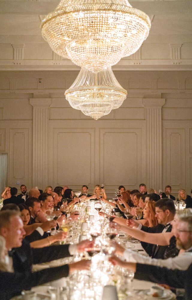 People clink their glasses across a candlelit table, toasting the New Year and congratulating the newlywed couple on their New Year's Eve wedding.