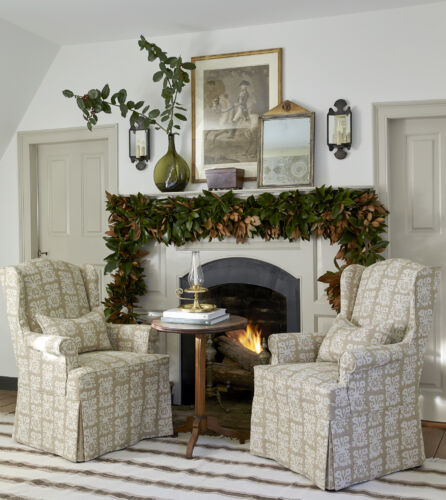 A white fireplace is decorated with magnolia leaves.