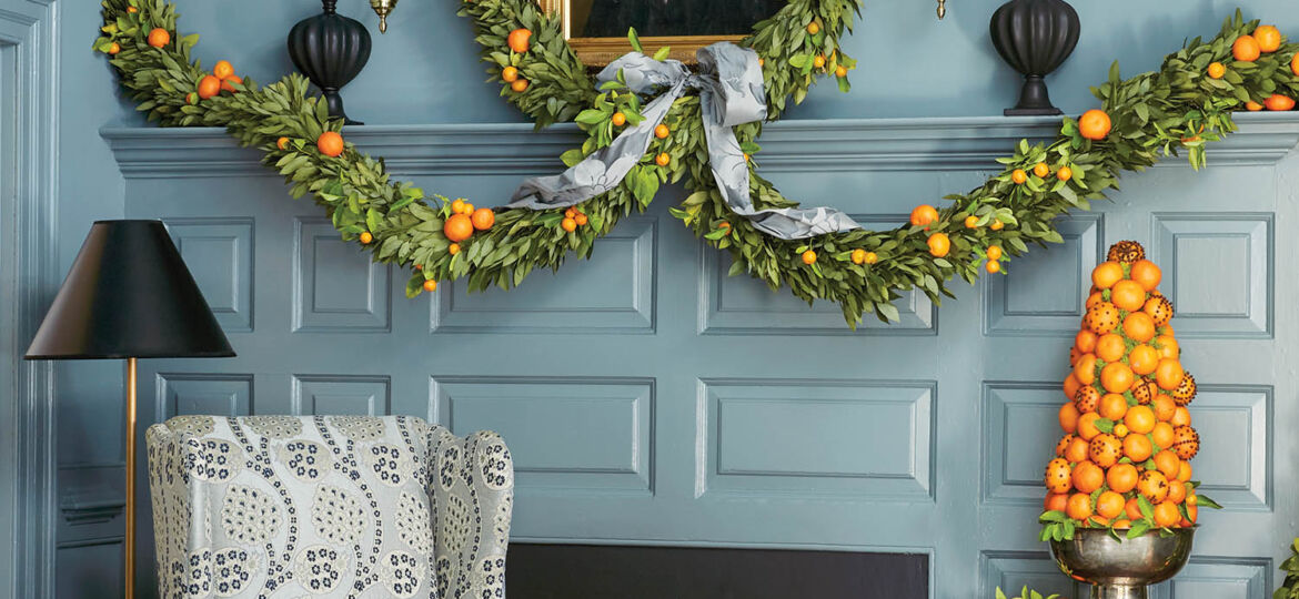 A blue room and fireplace mantel are decorated with greenery and oranges.
