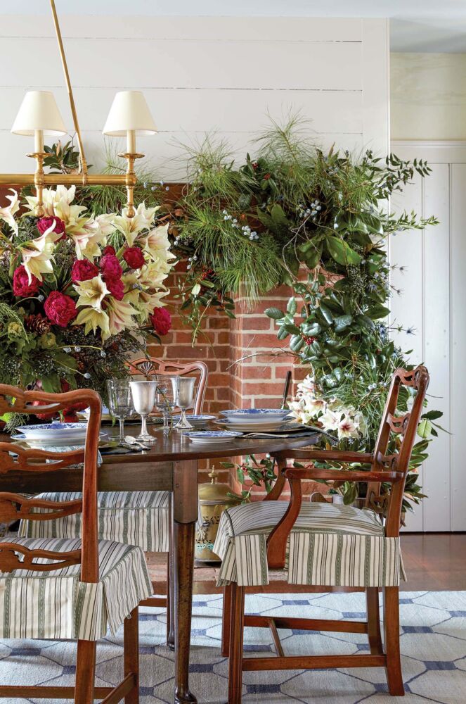 A simply decorated dining room table sits in front of a brick fireplace is decorated in greenery.