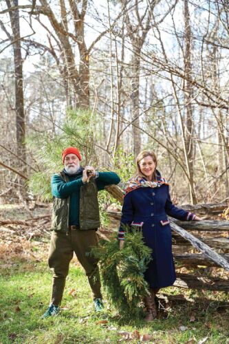 A man and woman stand in a forest holding foraged branches.