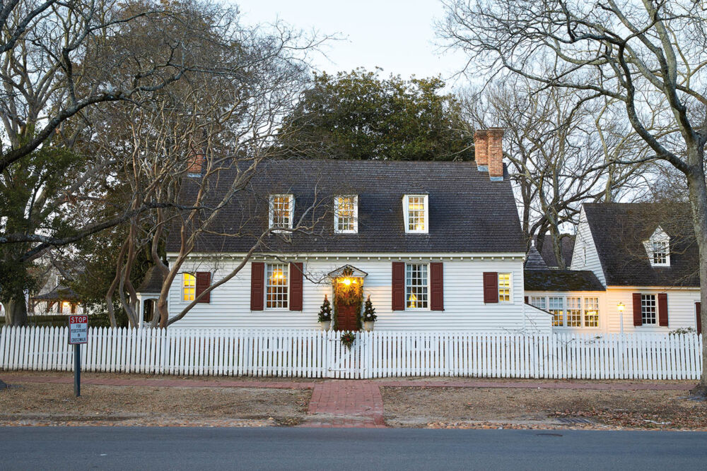 A white colonial house is dimly lit and surrounded by bare trees.