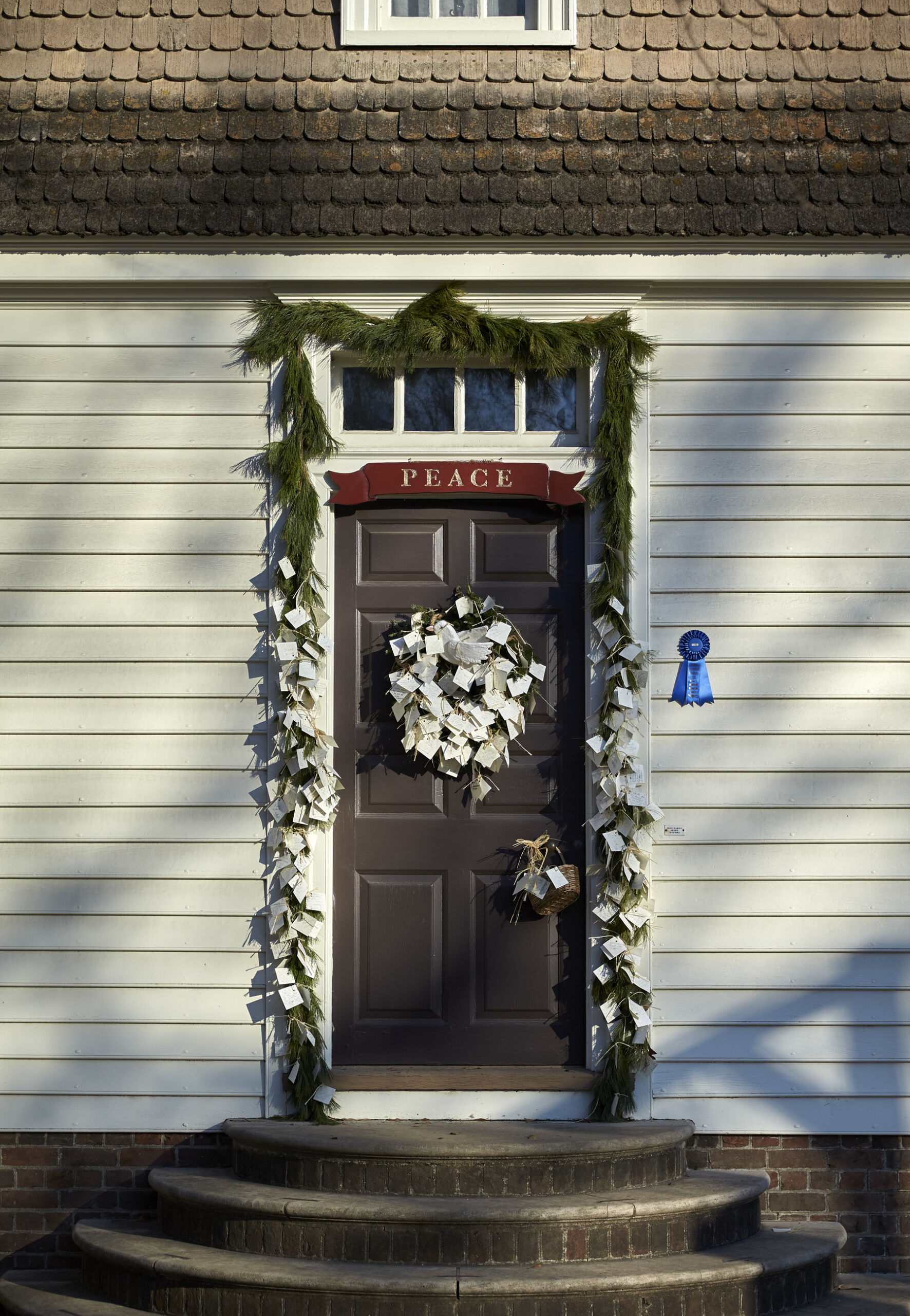 A wreath decorated with white paper envelopes decorates a brown front door.