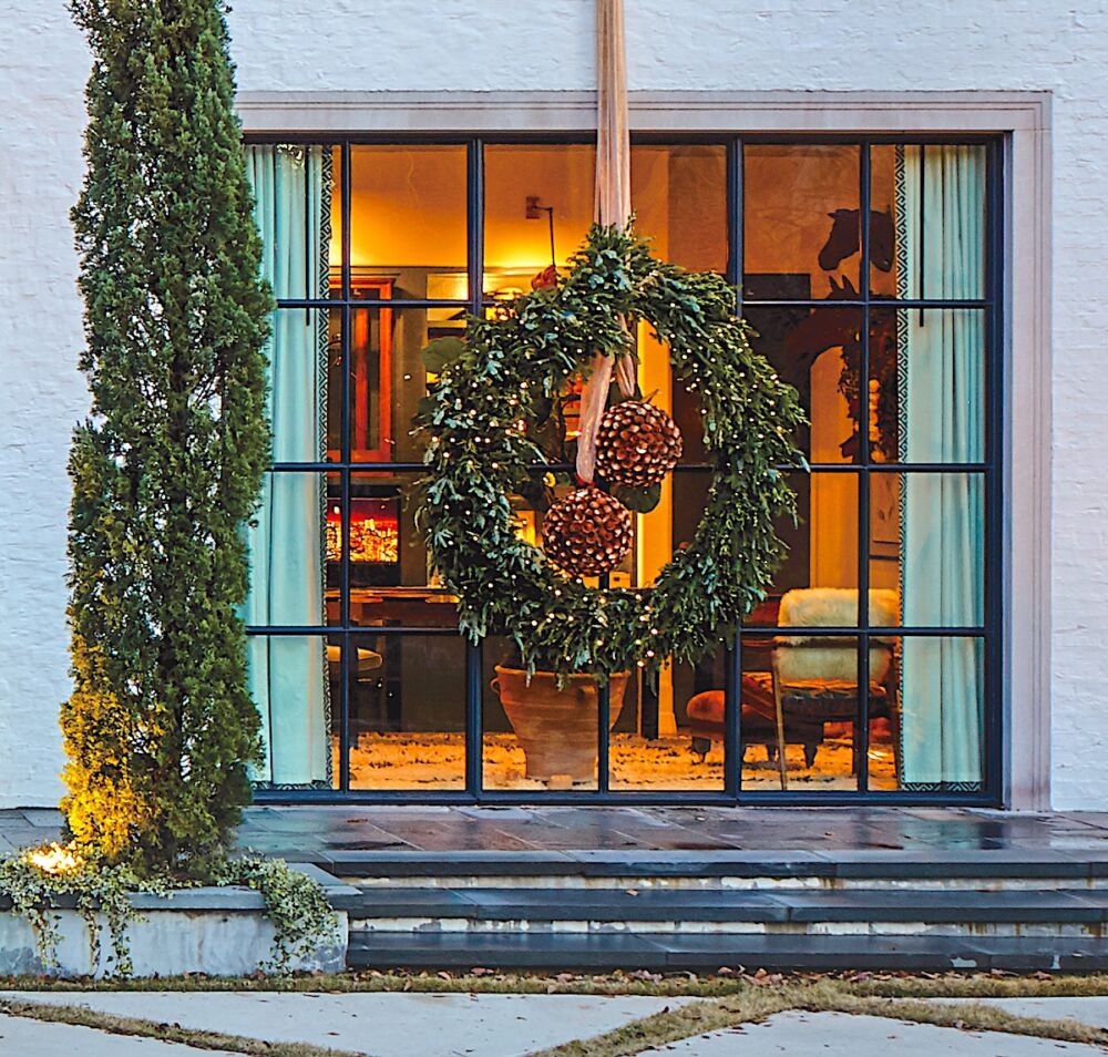 Giant holiday wreath with twinkle lights hanging from rose-colored ribbon provides striking Christmas window decor.