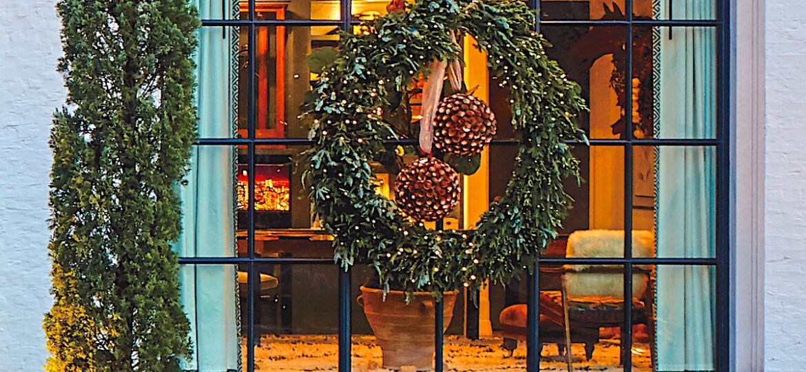 Giant holiday wreath with twinkle lights hanging from rose-colored ribbon provides striking Christmas window decor.